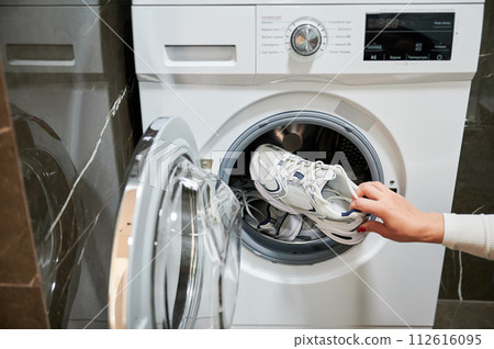 Dirty sport shoes need to be washed. Cropped photo of woman putting sneaker in washing machine. 112616095