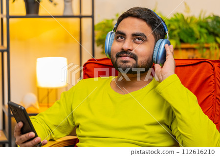 Happy relaxed man in wireless headphones dancing listening favorite disco pop music on home chair Happy relaxed man in wireless headphones dancing listening favorite disco pop music on home chair 112616210