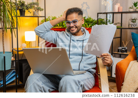 Stressed angry Indian man looking at unpaid bank debt loan bills, doing paperwork planning budget 112616238