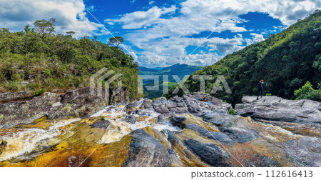 Hiker Overlooking a Scenic Waterfall and Lush Mountains 112616413