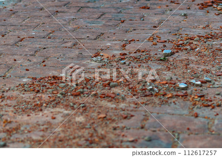 Remains of construction debris on street paved with paving stones in form of red brick fragments, mortar. Losses, damages in production, construction, transportation, loading, unloading. Efficiency Remains of construction debris on street paved with paving stones in form of red brick fragments, mortar. Losses, damages in production, construction, transportation, loading, unloading. Efficiency 112617257