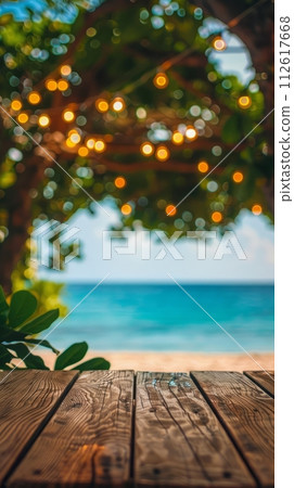 Empty wooden planks table against a blurred background with a sea coast with palm trees and glowing light bulbs in the evening 112617668
