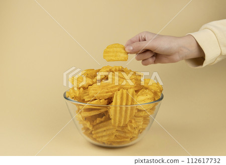 The hand takes potato chips from the glass bowl. The hand with the chips. 112617732