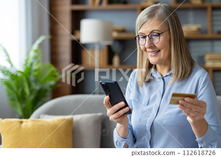 Mature woman holding credit card and smartphone, purchasing online from the comfort of home. Mature woman holding credit card and smartphone, purchasing online from the comfort of home. 112618726