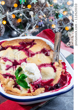 Berry cobbler in enamel baking dish, with ice cream, Christmas decoration with bokeh, vertical 112620010