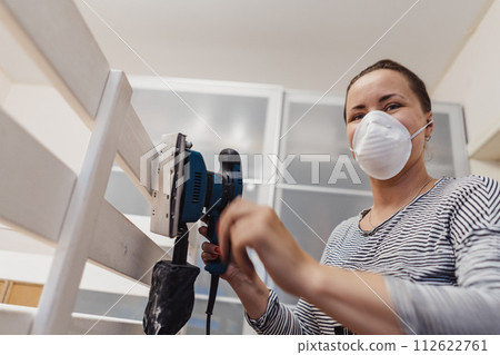 woman rubs wooden child bed with power sander or grinder removing old paint 112622761