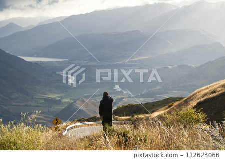 Man taking photograph of beautiful river valley surrounded by mountains with his phone, New Zealand Man taking photograph of beautiful river valley surrounded by mountains with his phone, New Zealand 112623066