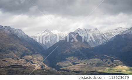 View on snowy mountains rising from green pastures during overcast cloudy day, New Zealand View on snowy mountains rising from green pastures during overcast cloudy day, New Zealand 112623079