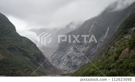 Wide shot of massive glacier flowing into a valley through steep rock walls shot in New Zealand Wide shot of massive glacier flowing into a valley through steep rock walls shot in New Zealand 112623098