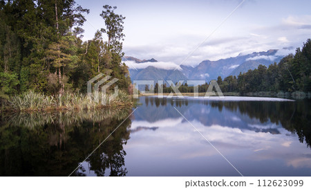 Beautiful lake surrounded by exotic forest and mountains in background during sunset, New Zealand Beautiful lake surrounded by exotic forest and mountains in background during sunset, New Zealand 112623099