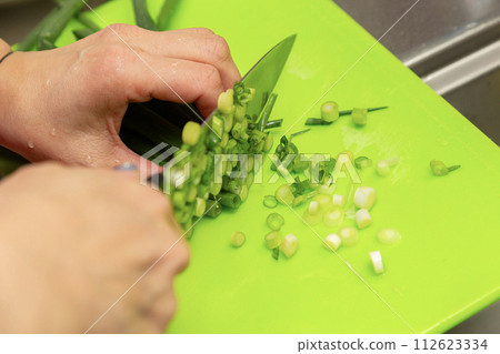 Hands of a woman cutting green onions Hands of a woman cutting green onions 112623334