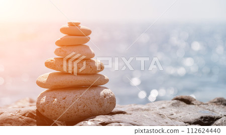 Pyramid stones on the seashore on a sunny day on the blue sea background. Happy holidays. Pebble beach, calm sea, travel destination. Concept of happy vacation on the sea, meditation, spa, calmness. Pyramid stones on the seashore on a sunny day on the blue sea background. Happy holidays. Pebble beach, calm sea, travel destination. Concept of happy vacation on the sea, meditation, spa, calmness. 112624440