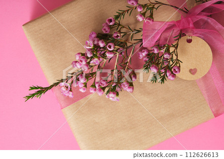 Brown craft gift box with empty circle tag, waxflower on pink background. Place for your text 112626613
