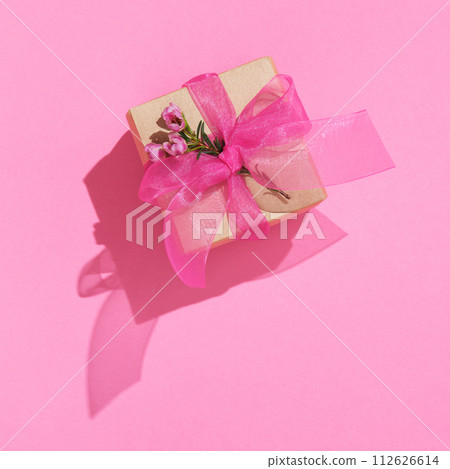 Craft brown gift box with pink ribbon and waxflowers on pink background 112626614