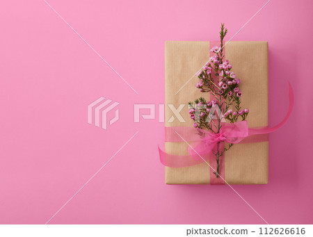 Craft brown gift box with pink ribbon and waxflowers on magenta background with space for your text 112626616