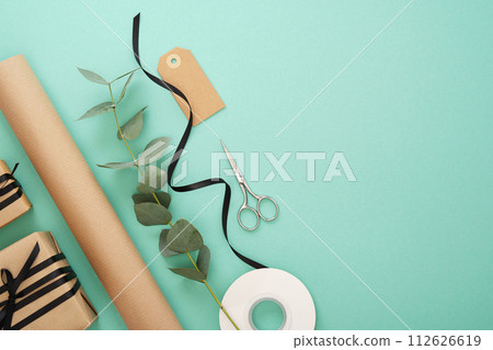 Gift wrapping. Brown craft wrapping paper, black ribbon, scissors, eucalyptus, tags. Mint background. Copyspace Gift wrapping. Brown craft wrapping paper, black ribbon, scissors, eucalyptus, tags. Mint background. Copyspace 112626619