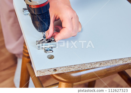 Adjustable hinges are installed in the chipboard cabinet door during flat pack furniture assembly. Adjustable hinges are installed in the chipboard cabinet door during flat pack furniture assembly. 112627323