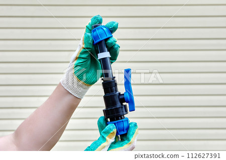 Installation of pipeline joint with ball valve using compression clamps, gloved hands on striped background of house wall. Installation of pipeline joint with ball valve using compression clamps, gloved hands on striped background of house wall. 112627391