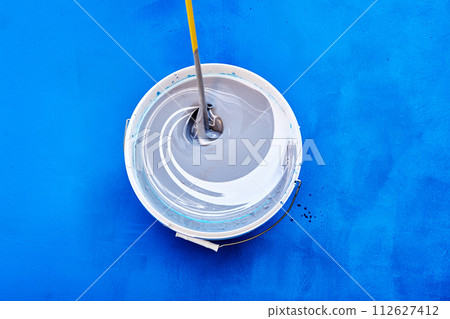 Stirring rod mixing and tinting paint for walls, house painter tinted paint in bucket on blue background. 112627412