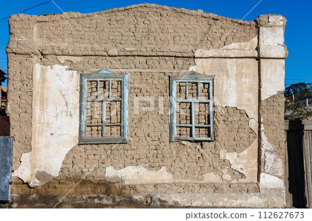 old house adobe air brick wall with two embedded wooden window frames and peeled off plaster leftovers - flat texture 112627673