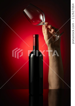 Unopened bottle of red wine and hands wine glass. 112627864