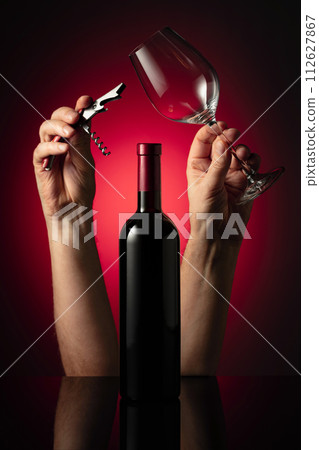 Unopened bottle of red wine and hands with corkscrew and wine glass. 112627867