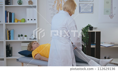 A certified orthopedist examines the knee of her patient, making a diagnosis in physiatry 112629136