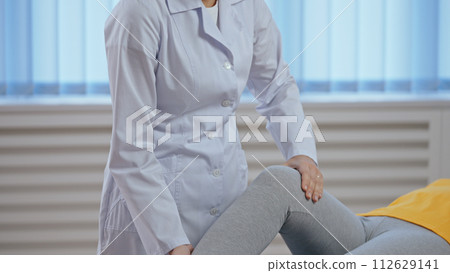 Close-up of an orthopedist examining a patient's knee movability, working as a rehabilitation physician 112629141