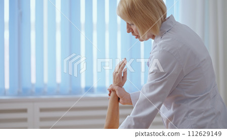 A qualified orthopedist tests the movability of a female patient's hand after treatment 112629149