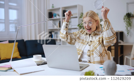 Senior woman receiving good news while working on laptop, unexpected surprise Senior woman receiving good news while working on laptop, unexpected surprise 112629209