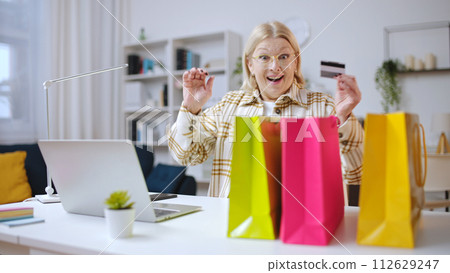 Happy woman ordering goods online, surprised with fast delivery, shopping bags on a table Happy woman ordering goods online, surprised with fast delivery, shopping bags on a table 112629247