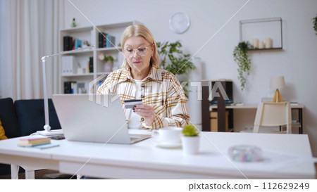 Mature woman entering credit card number, doing shopping online and ordering delivery Mature woman entering credit card number, doing shopping online and ordering delivery 112629249