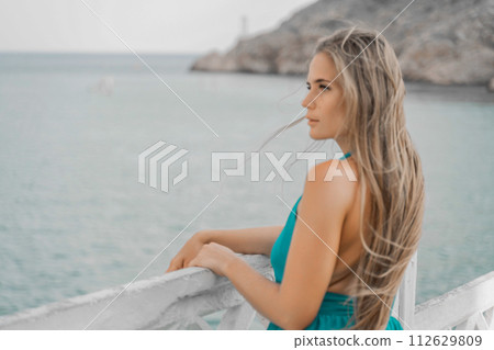 Woman sea green dress. Side view a happy woman with long hair in a long mint dress posing on a beach with calm sea bokeh lights on sunny day. Girl on the nature on blue sky background. Woman sea green dress. Side view a happy woman with long hair in a long mint dress posing on a beach with calm sea bokeh lights on sunny day. Girl on the nature on blue sky background. 112629809