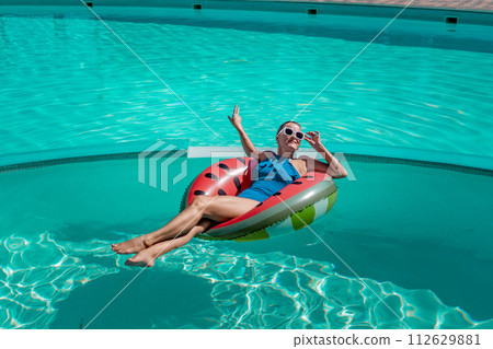 Happy woman in a swimsuit and sunglasses floating on an inflatable ring in the form of a watermelon, in the pool during summer holidays and vacations. Summer concept. 112629881