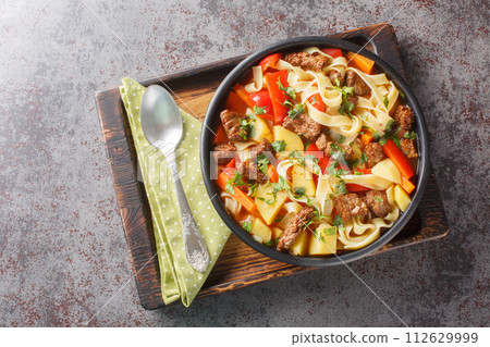 Laghman hand-pulled noodles in tomato and lamb stew closeup on the plate on the wooden board. Horizontal top view 112629999