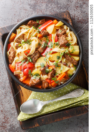 Lagman Uzbek dish is a fragrant soup with noodles and pieces of lamb, vegetables and herbs closeup on the plate. Vertical top view Lagman Uzbek dish is a fragrant soup with noodles and pieces of lamb, vegetables and herbs closeup on the plate. Vertical top view 112630005