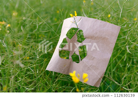 recycling logo, promoting environmental awareness. Eco sign. Cut paper with the logo of recycling on rapeseed. Recycling concept. Pollution of the planet. Out of focus recycling logo, promoting environmental awareness. Eco sign. Cut paper with the logo of recycling on rapeseed. Recycling concept. Pollution of the planet. Out of focus 112630139