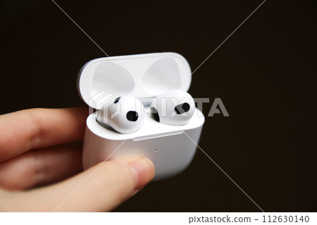 Hand holding white headphones in case on black background. Close up. Audio equipment, technology, music accessories, sound quality. Out of focus Hand holding white headphones in case on black background. Close up. Audio equipment, technology, music accessories, sound quality. Out of focus 112630140