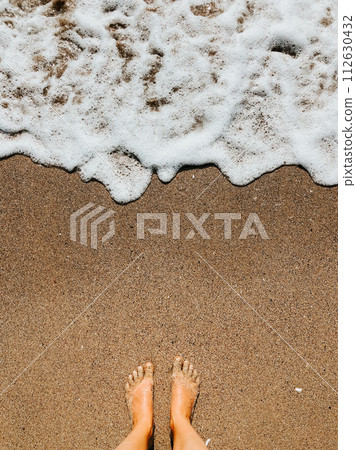 Woman legs barefoot at sea foam waves on sand beach summer day. top view above women feet. 112630432