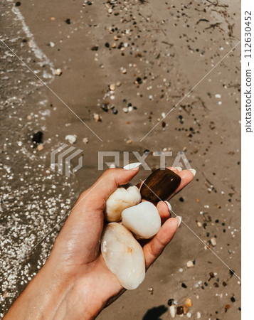 Woman hand manicure holding white beautiful stones above sea sandy summer beach. 112630452