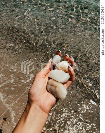 Woman hand manicure holding white beautiful stones above sea sandy summer beach. 112630454