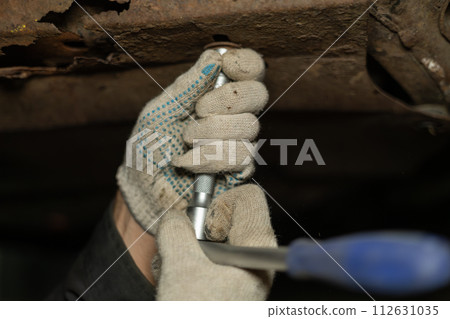 A mechanic in a hole under a car unscrews nuts in a garage while repairing a car. The mechanic unscrews the nuts removing the protection from the car to drain the old oil from the car. A mechanic in a hole under a car unscrews nuts in a garage while repairing a car. The mechanic unscrews the nuts removing the protection from the car to drain the old oil from the car. 112631035