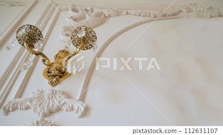 Decorative vintage wall lamp with two lamps, close-up. Lamp, bronze vintage sconce on a white wall. Vintage sconce with white glass shades. 112631107