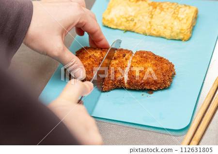 Hand of a woman cutting pork cutlet for lunch box 112631805