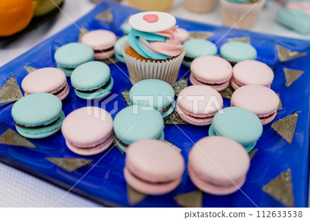 Colorful macarons and cupcakes arranged on blue festive tray Colorful macarons and cupcakes arranged on blue festive tray 112633538