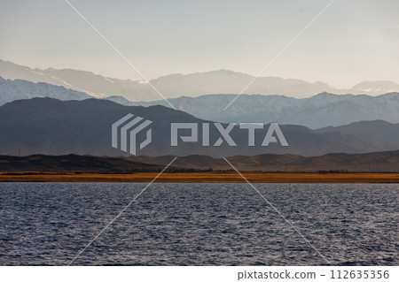 Blue calm water in Issyk-Kul lake with mountains on background at autumn afternoon 112635356