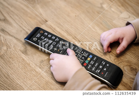 Child is watching TV. A child with a TV remote control in front of the screen. 112635439