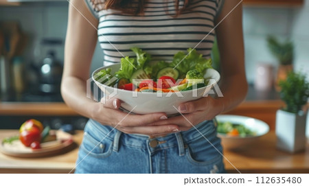 Woman holding a bowl of greens and vegetables 112635480