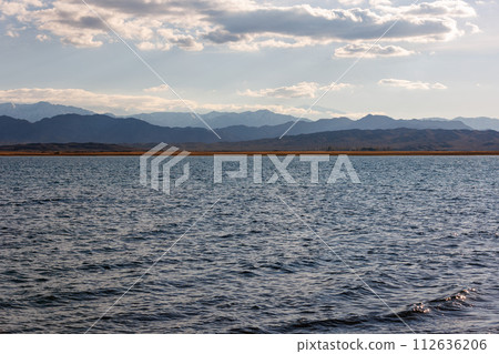 Blue calm water in Issyk-Kul lake with mountains on background at autumn afternoon 112636206