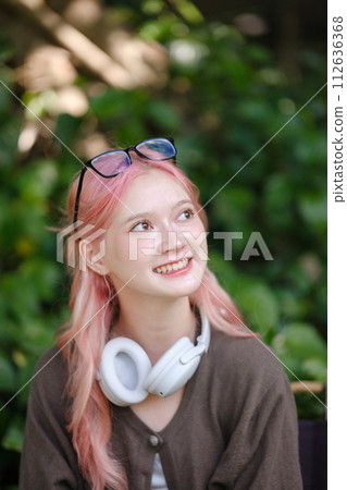 A cute pink-haired girl drawing on a digital tablet and wearing headphones in the garden, a Woman Doing Freelance Work in the Garden, and a woman with a digital tablet with artwork. 112636368